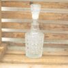 Elegant glass decanter with geometric patterns, set in a rustic wooden crate. Perfect home accent.
