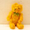 Charming vintage yellow teddy bear with green bow, exuding nostalgia and warmth. Perfect cuddle companion!