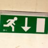 Green emergency exit sign with running figure and downward arrow for quick evacuation guidance.