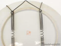 Vintage porcelain wall plate with a red mark and coiled wire hanger for decor.
