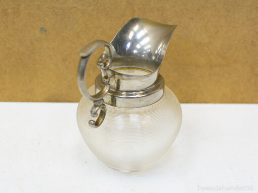Elegant vintage glass pitcher with a metallic spout and handle, ideal for serving or decor.