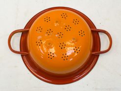 Bright orange metal colander with stylish handles, ideal for draining pasta and vegetables.