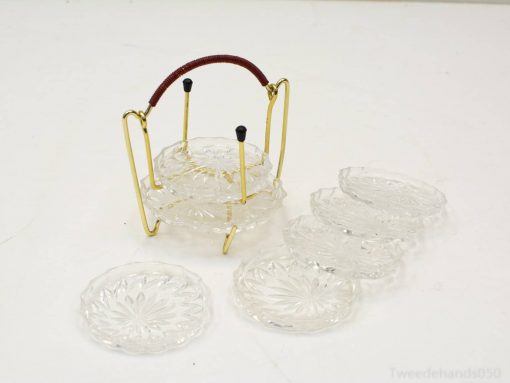 Elegant glass coasters with gold holder and leather grip for sophisticated table settings.