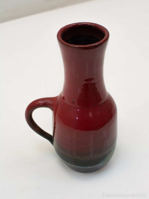 Elegant deep red ceramic pitcher with a glossy finish and graceful handle, perfect for decoration.