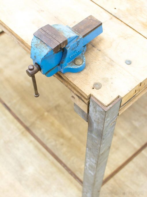 Sturdy blue vise on a rustic wooden workbench, perfect for skilled craftsmanship and projects.