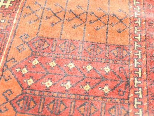 Colorful vintage rug with geometric patterns in warm red and orange tones.
