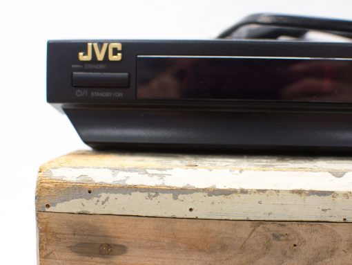 Vintage JVC DVD player on weathered wood, blending nostalgia with modern design.