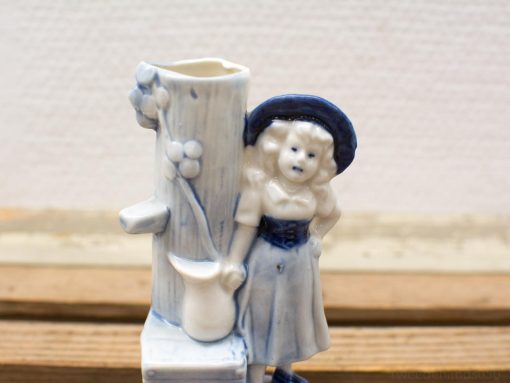 Charming ceramic girl figurine by tree stump, evoking nostalgia and folk art beauty.