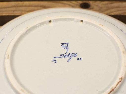 Antique hand-painted blue and white ceramic plate with decorative holes and intricate markings.