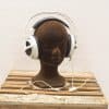 Modern white headphones on a dark mannequin head atop rustic wooden platform.
