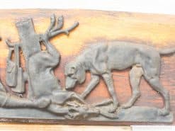 Wood relief carving of a hunting scene with a dog and deer, showcasing intricate craftsmanship.