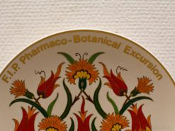Botanical decorative plate from 1987, featuring vibrant flowers and F.I.P. Pharmaco-Botanical Excursion.
