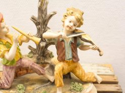 Whimsical figurine of two joyful boys playing music together with a violin and flute.