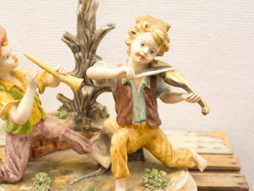 Whimsical figurine of two joyful boys playing music together with a violin and flute.