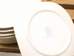 Elegant white ceramic plates with a crown logo, perfect for fine dining and special occasions.