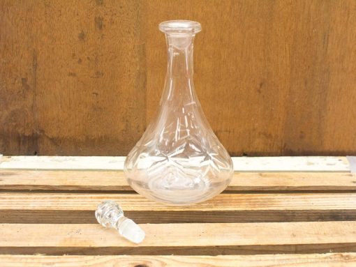 Elegant glass decanter with stopper on rustic wood, perfect for serving wine or spirits.