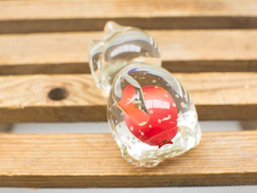 Elegant glass sculpture with a red apple on a warm wooden surface.