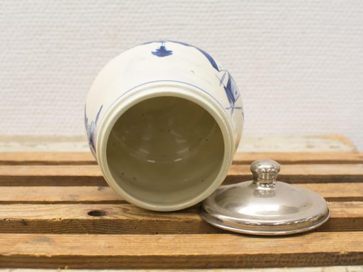 Glossy white ceramic jar with blue maritime designs and metallic lid on rustic wood.