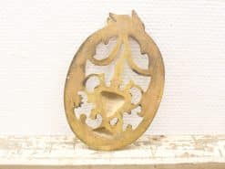 Antique brass ornament with intricate floral designs and a vintage oval shape.