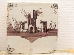 Hand-painted ceramic tile featuring rustic architecture and organic motifs in warm earth tones.