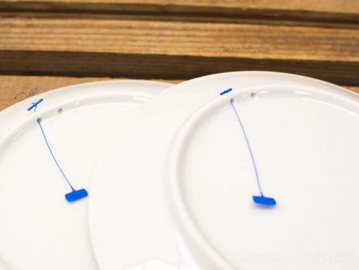Elegant white plates on a rustic wooden table, featuring intriguing blue markings beneath.