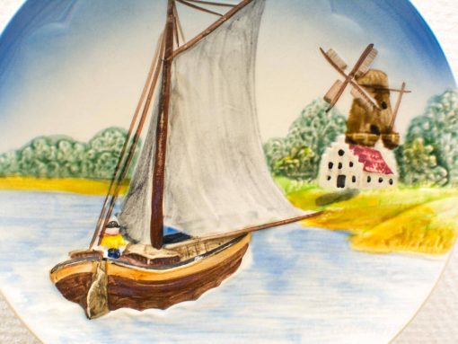 Charming ceramic plate featuring a sailboat, lush greenery, and a quaint windmill scene.