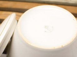 Vintage white ceramic cup base with logo on rustic wooden background.