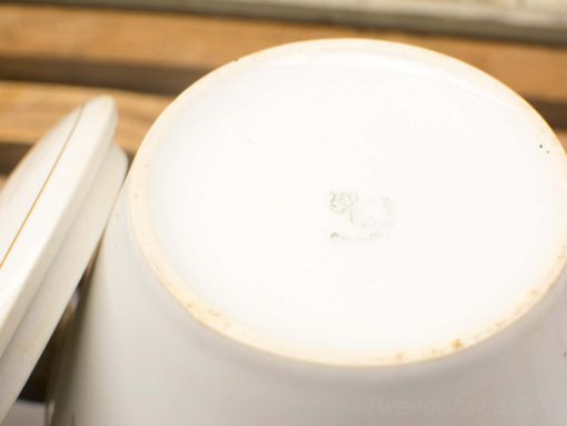 Vintage white ceramic cup base with logo on rustic wooden background.