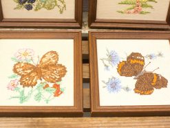 Charming vintage needlework featuring vibrant butterflies and floral designs in rustic frames.