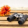 Vintage binoculars with a vibrant artificial flower, perfect for outdoor adventures and home decor.
