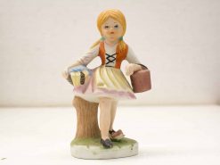 Charming porcelain figurine of a girl with a book and basket, evoking childhood nostalgia.