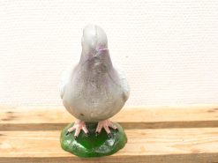 Whimsical gray and purple pigeon sculpture with detailed pink legs on a grassy base.
