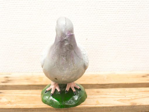 Whimsical gray and purple pigeon sculpture with detailed pink legs on a grassy base.