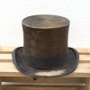 Vintage brown top hat on rustic wooden palette, showcasing timeless elegance and historical charm.