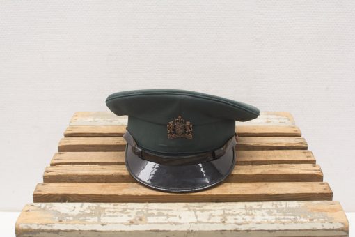 Elegant green military cap with crown emblem on rustic wooden base, showcasing craftsmanship and tradition.