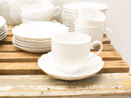 Elegant white teacup and saucer set on rustic wood, perfect for tea parties.