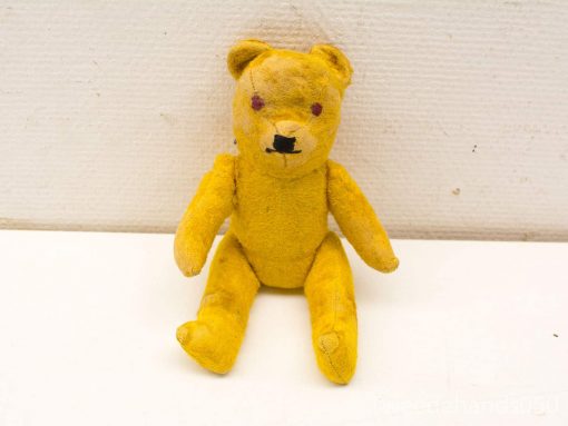 Charming vintage yellow teddy bear with purple eyes and frayed fabric, perfect for collectors.