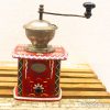 Charming vintage red coffee grinder with ornate designs, polished metal bowl, and functional drawer.