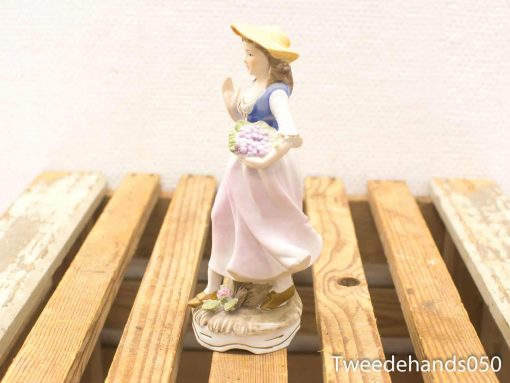 Charming porcelain figurine of a young woman in pastoral attire with flowers.