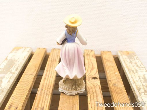 Charming porcelain figurine of a girl in traditional dress and straw hat, celebrating rural beauty.