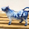 Charming Delft Blue cow creamer, handcrafted with intricate windmill designs, perfect for decor or use.