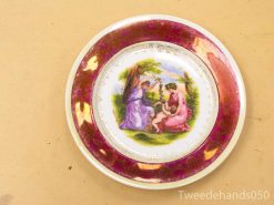 Elegant decorative plate featuring two women in a lush garden, framed in maroon and gold.