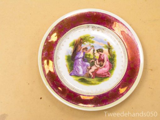 Elegant decorative plate featuring two women in a lush garden, framed in maroon and gold.
