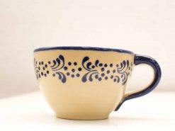 Elegant beige ceramic cup with navy blue floral patterns and comfortable handle for hot beverages.