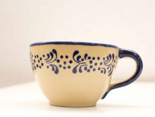 Elegant beige ceramic cup with navy blue floral patterns and comfortable handle for hot beverages.