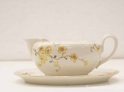 Elegant porcelain gravy boat and saucer with floral design, perfect for formal dining.