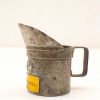 Vintage metal measuring cup with patina and yellow label, perfect for retro kitchen decor.