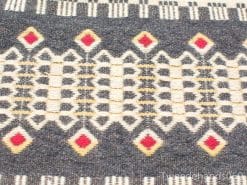 Handwoven tablecloth featuring vibrant geometric patterns on a rich charcoal gray background.
