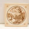Charming vintage ceramic tile featuring a serene river landscape with sailboats and quaint homes.