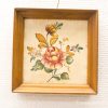 Vintage floral artwork in warm wood frame, featuring a rose and vibrant leaves.